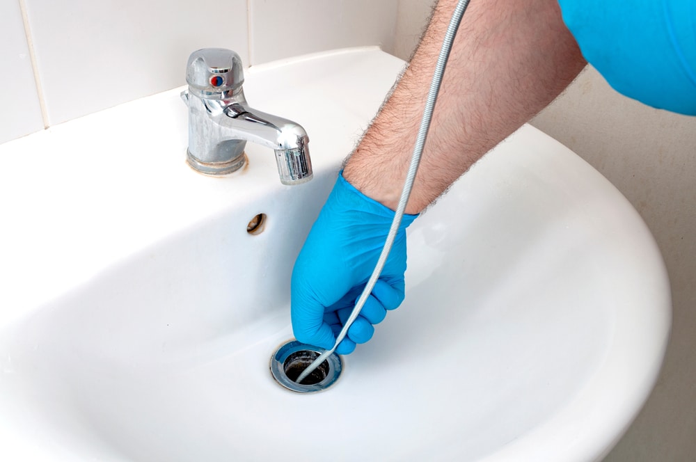 A plumber cleaning a drain with a tool.