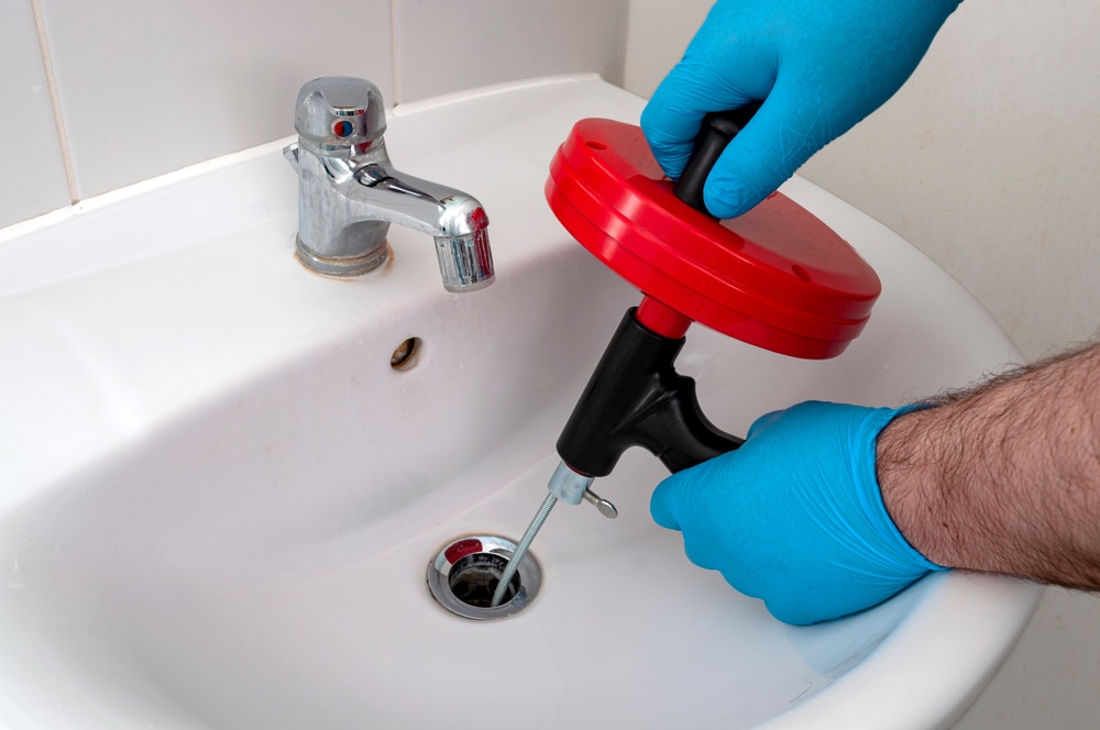 A plumber using a drain snake to remove a clog from a kitchen sink drain.