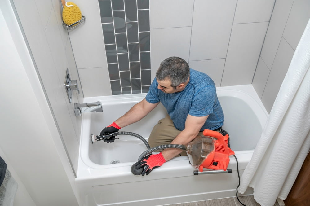 Professional plumber using a drain snake to clear a clogged drain